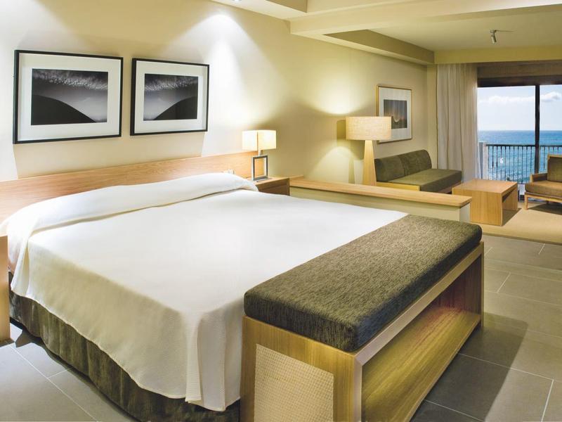 Chambre d'hôtel moderne avec grand lit et vue sur la mer à travers de grandes fenêtres.