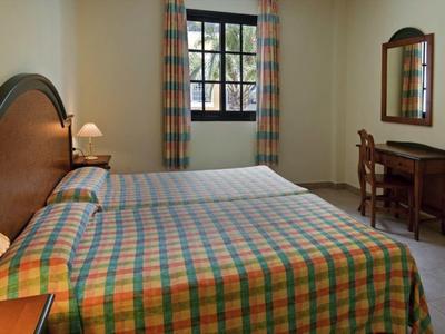 Hotelkamer met twee bedden, geruit beddengoed, houten meubels en een raam met gordijnen.