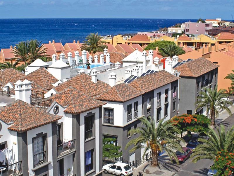 Uitzicht op een woonwijk met rode daken en de zee op de achtergrond onder een heldere lucht.