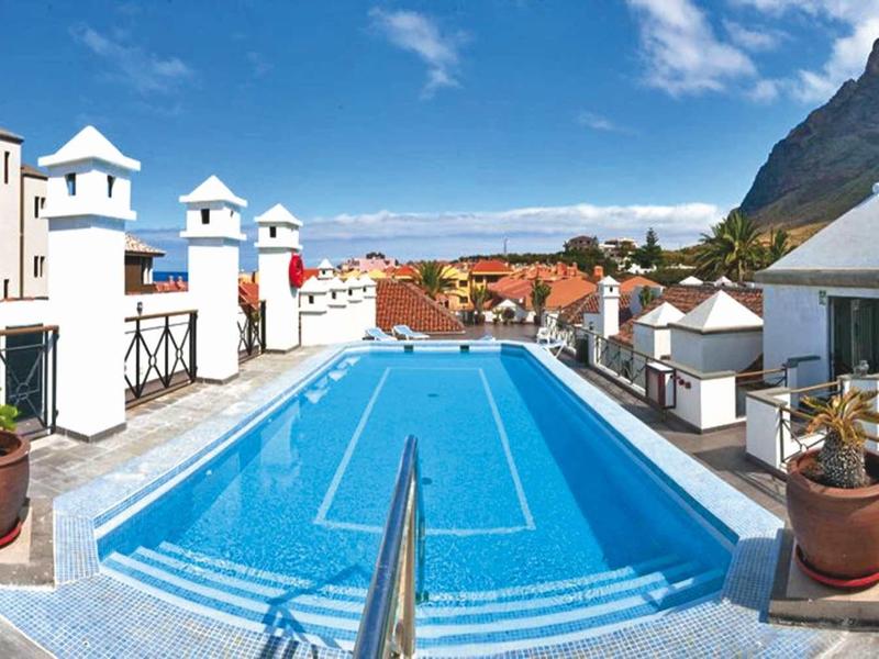 Zwembad op het dak met uitzicht op witte gebouwen en bergen op de achtergrond.