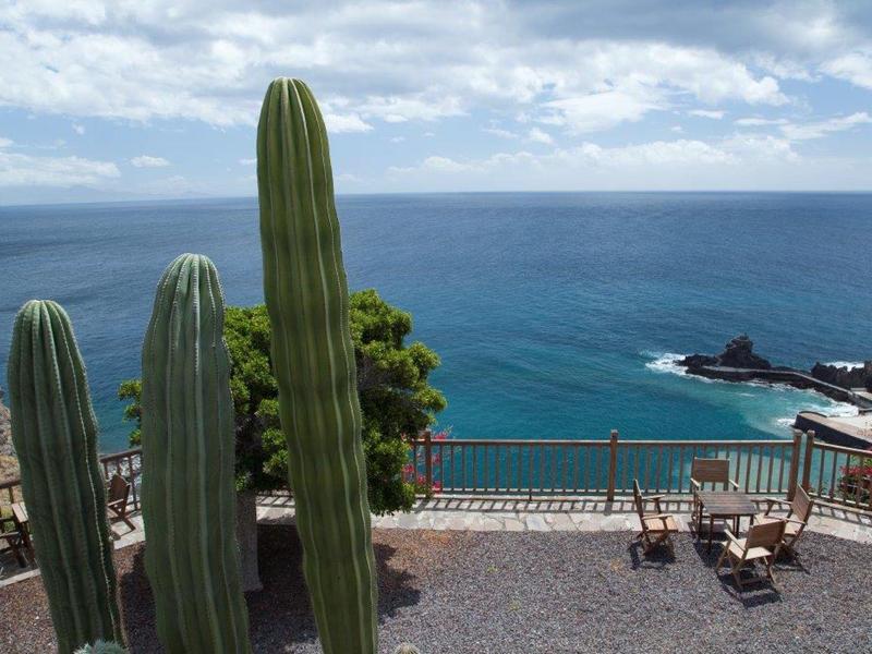 Terrazza con sedie e cactus di fronte al mare blu e cielo nuvoloso.