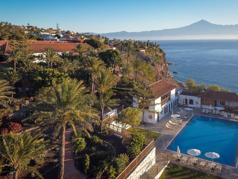 Vista di una piscina di un hotel su una scogliera con oceano e montagne sullo sfondo.