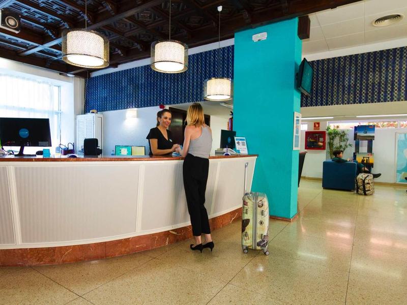 Moderne Rezeption mit weißem Tresen, zwei Frauen im Gespräch, helles, offenes Büro mit blauen Akzenten.