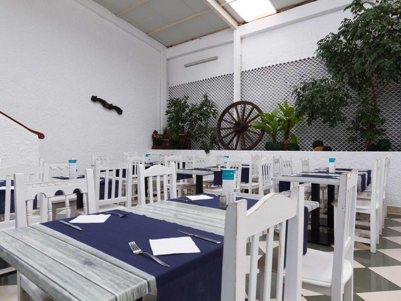 Weiß gestrichene Holzstühle und Tische mit blauen Tischdecken in hellem, schlichtem Restaurant.