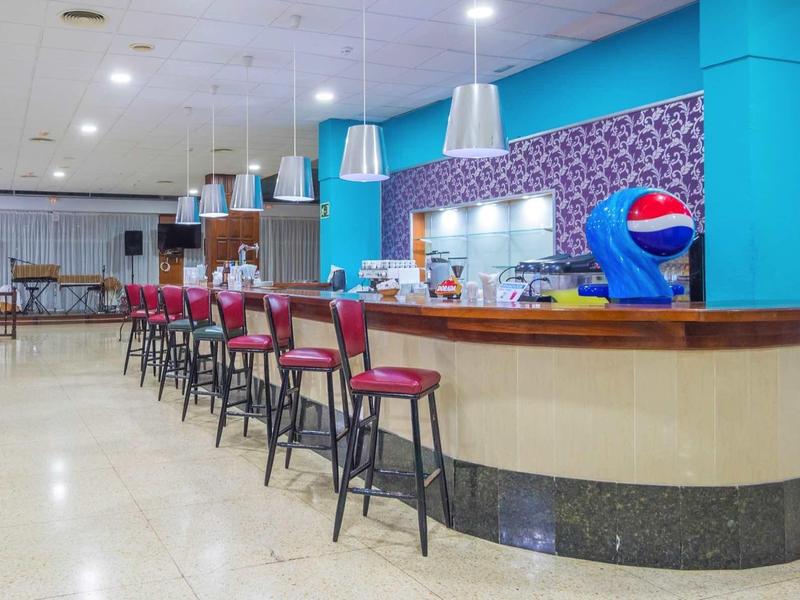 Moderner Barbereich mit roten Barhockern, blauer Wand und buntem Fliesenspiegel, heller Raum.