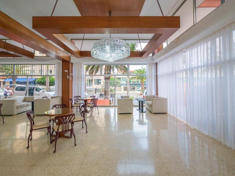 Großer, heller Raum mit Holzdeckenbalken, Kronleuchter, weißen Vorhängen und verstreuten Tischen mit Stühlen.