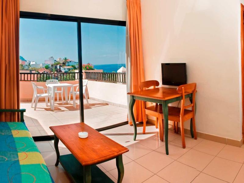 Lichte hotelkamer met zithoek, bureau en balkon met uitzicht op bergen.