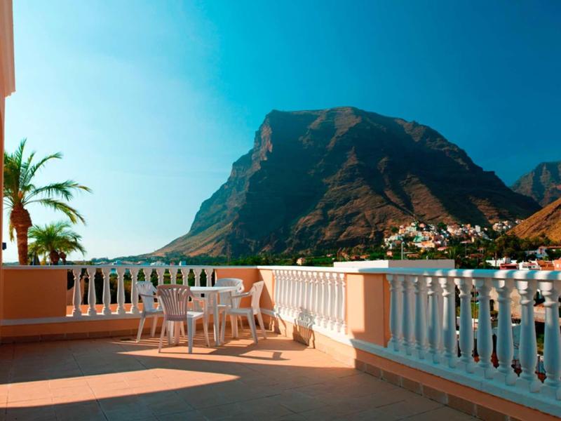 Zonnig terras met wit hek, tafel en stoelen tegen berg en blauwe lucht