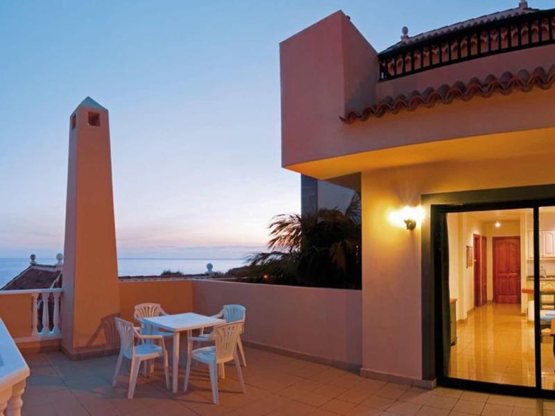 Groot terras met tafel en stoelen voor een vakantiehuis bij zonsondergang.