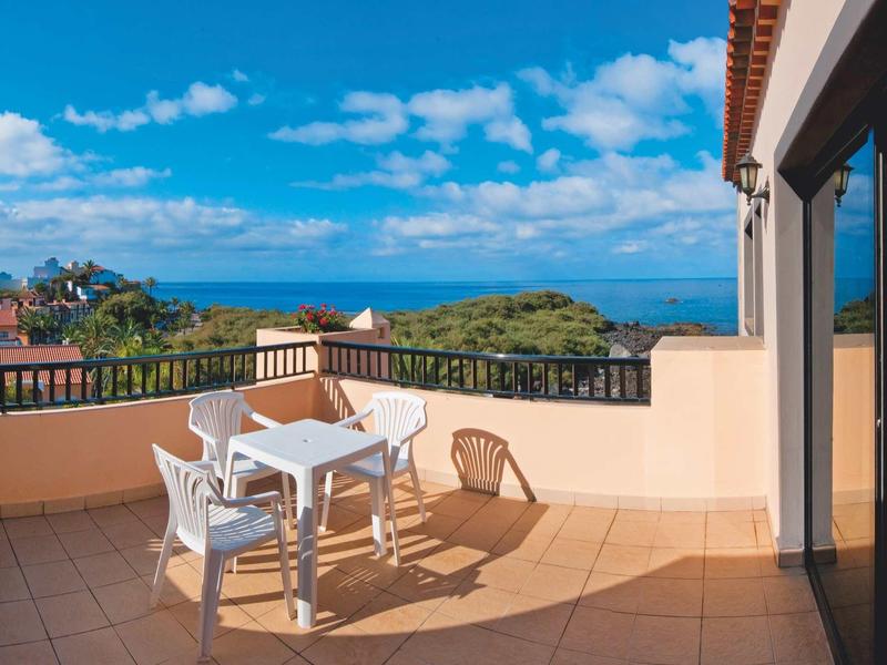 Balkon met plastic stoelen en tafel met uitzicht op zee onder een heldere lucht.