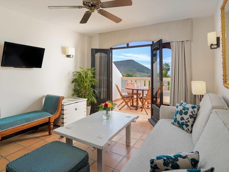 Jasny salon z wygodnymi miejscami do siedzenia, otwartym balkonem i widokiem na górski krajobraz.