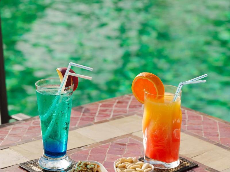 Dwa kolorowe mieszane napoje z rurkami i dekoracją, podane z przekąskami na mozaikowym stole.