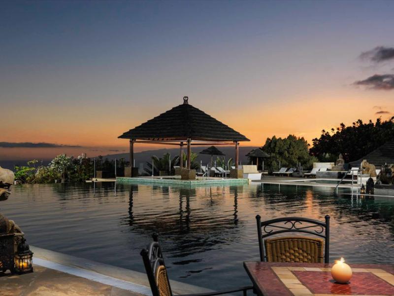 Basen infinity z pawilonem i miejscem do siedzenia o zachodzie słońca w ośrodku.