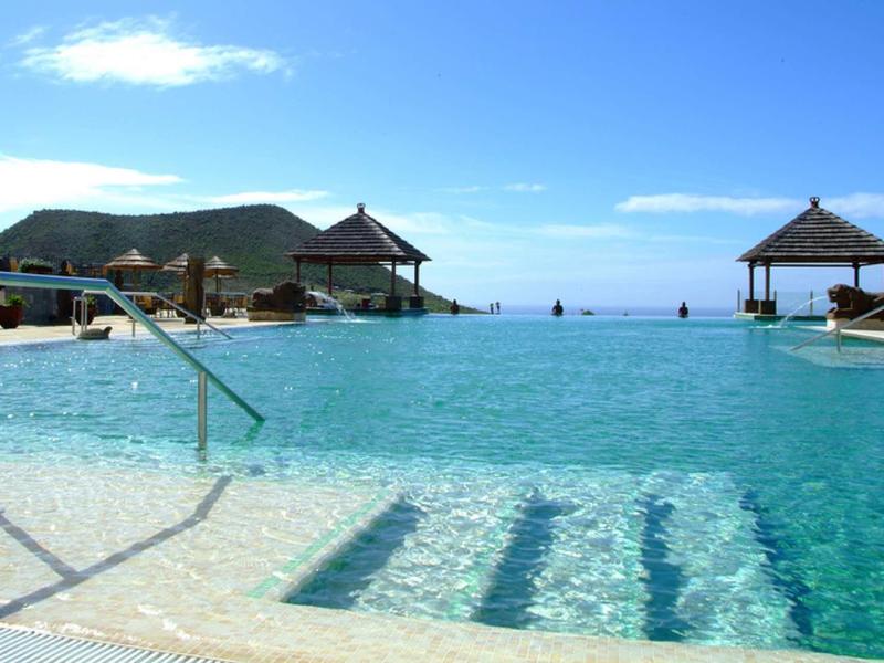 Basen infinity z schodkami i pawilonami z widokiem na morze pod czystym niebem.