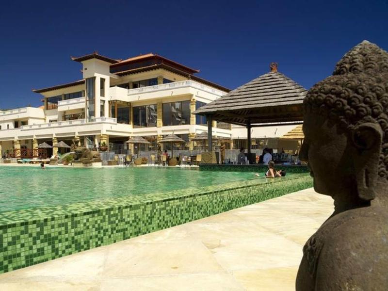 Posąg Buddy obok dużego basenu z budynkiem hotelu w tle przy czystym niebie.