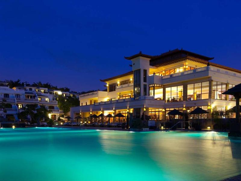 Oświetlony hotel z dużym basenem nocą pod czystym niebem.