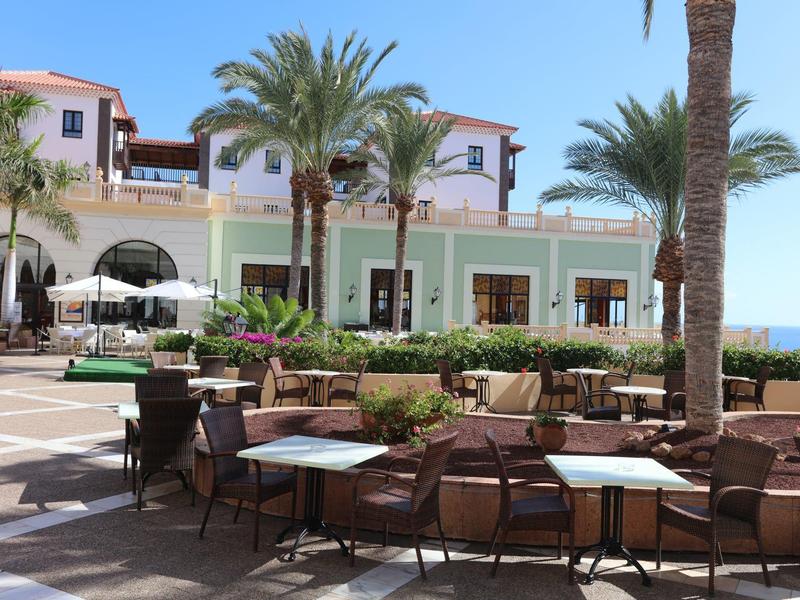 Terrazza di un hotel con aree salotto, palme e vista sul mare in una giornata soleggiata.
