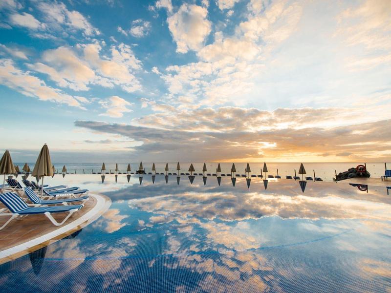 Una piscina d'hotel al tramonto con lettini e ombrelloni lungo il bordo.