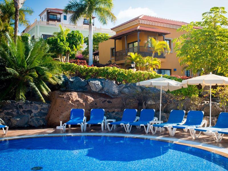 Piscina rotonda con lettini blu e vegetazione tropicale in un giardino d'hotel.
