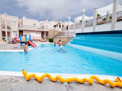 Moderner Außenpool mit blauen Wasser, umgeben von hellen Gebäuden und spielenden Kindern.