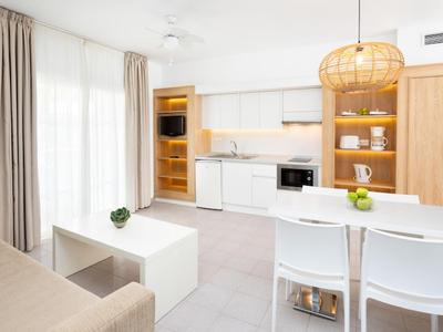 Helle, moderne Küche mit weißen Möbeln, Holzregalen, Esstisch, Sofa und natürlicher Beleuchtung.