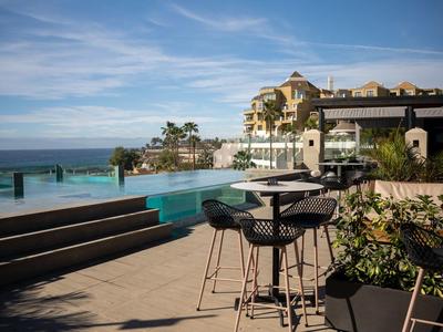 Unter freiem Himmel: Terrasse mit schwarzen Stühlen, Infinity-Pool und Meer im Hintergrund.