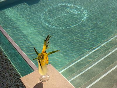 Cocktail mit Ananas und Minze vor türkisfarbenem Swimmingpool mit Treppenstufen.