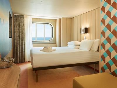 Modern eingerichtetes Hotelzimmer mit großem Bett und rundem Fenster mit Meeresblick.