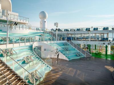Modernes, mehrstufiges Schwimmbaddeck auf einem Kreuzfahrtschiff bei Sonnenschein.