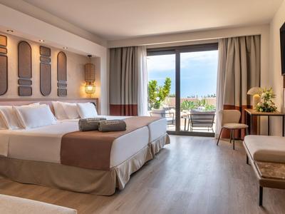 Modernes Hotelzimmer mit zwei Betten und Zugang zu einem Balkon mit Blick auf eine Stadt.