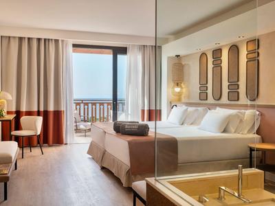 Modernes Hotelzimmer mit großem Bett, Balkon und hellem Holzboden.
