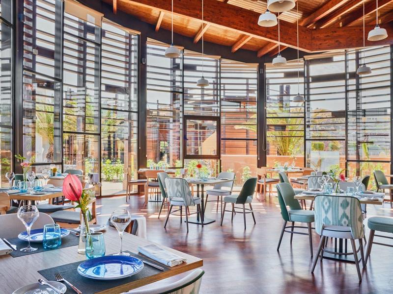 Helles, rundes Restaurant mit Holzboden, großen Fenstern und modernem Mobiliar in Pastellfarben.