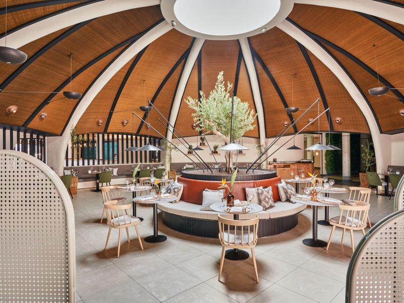 Rundes Restaurant mit Holzdach, weißem Mobiliar und zentralem Blumenarrangement.