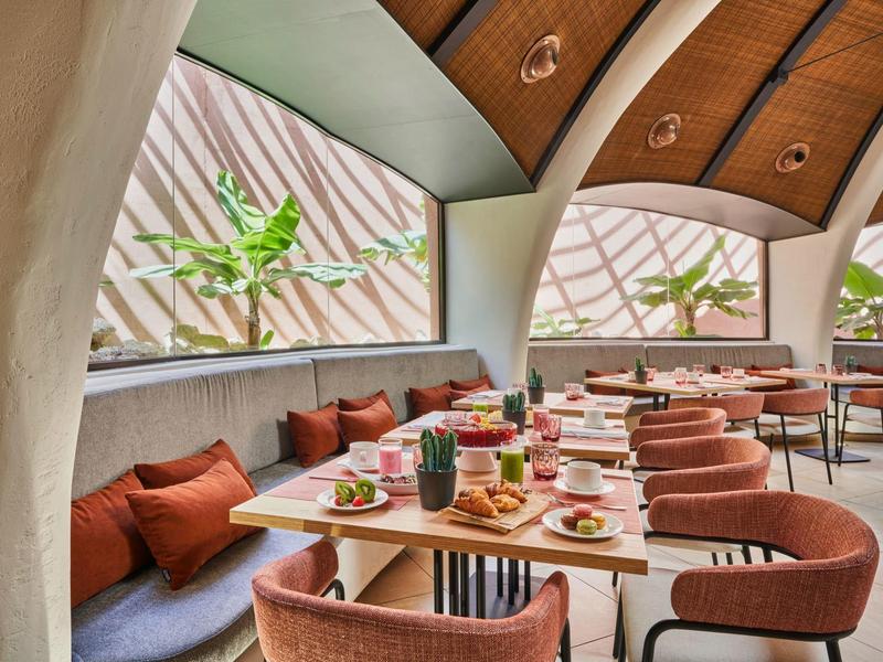 Modernes Café mit großen Fenstern, geschwungenen Decken und Beerenfarbenen Stühlen.