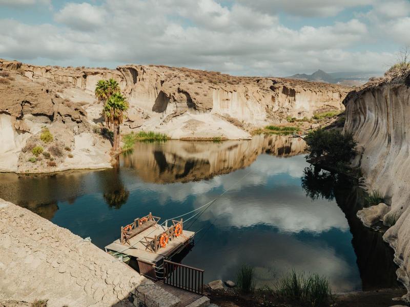 Schmaler Fluss fließt zwischen felsigen Klippen unter bewölktem Himmel, mit Holzboot am Ufer.