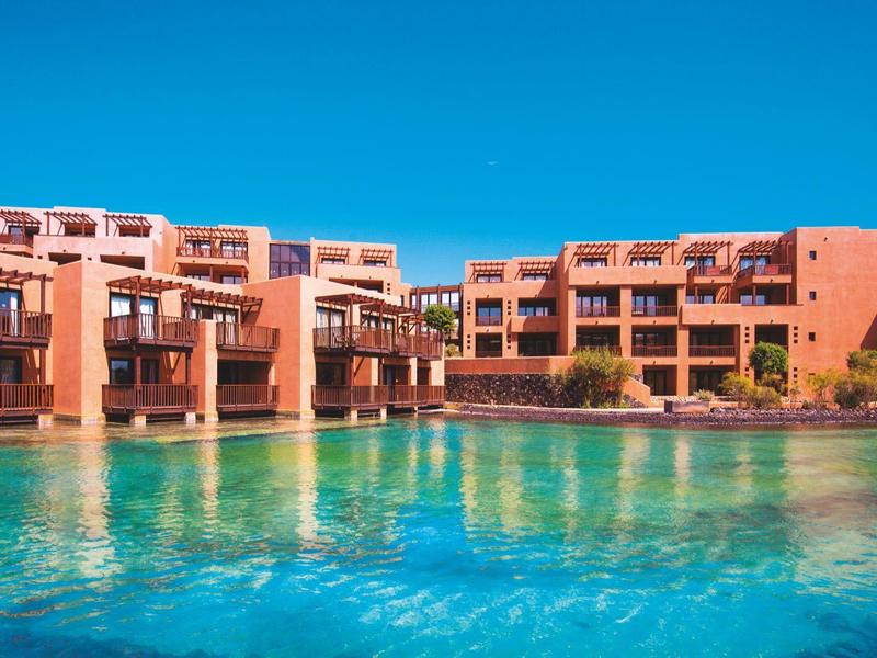 Großes modernes Hotel mit roten Gebäuden und Pool unter klarem blauem Himmel.