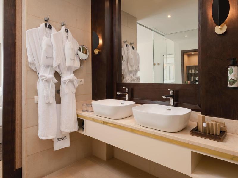 Modernes Badezimmer mit zwei weißen Waschbecken, braunen Wänden und weißen Bademänteln an der Wand.