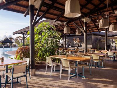 Open restaurant area with pool view and lounge chairs under wooden canopy.
