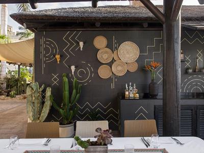 Buitenzitje met stoelen, cactus, decoratieve zwarte muur en rotanmanddecoratie.