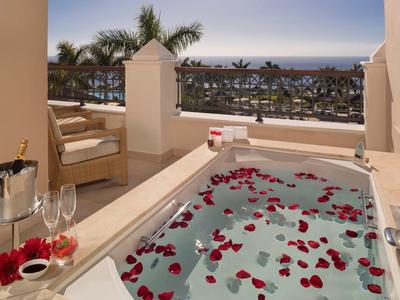 Bubbelbad met rozenblaadjes op een zonnig terras met uitzicht op zee en champagneglazen.