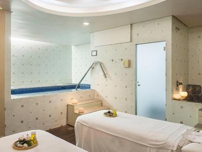 Lichte spa behandelkamer met twee massagetafels, grote spiegel en kleine whirlpool.