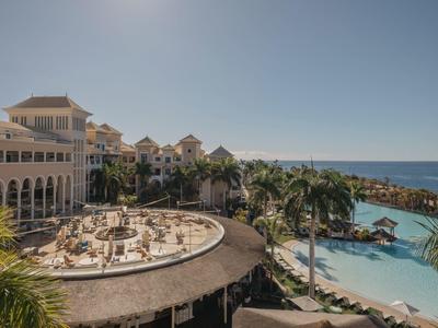 Luxe strandresort met zwembad, palmbomen en uitzicht op zee onder een heldere hemel.