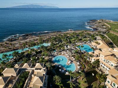 Luchtfoto van tropisch resort met zwembaden, palmbomen en uitzicht op zee.