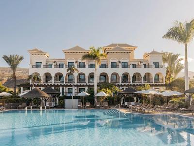 Luxe hotel met zwembad, palmbomen en parasols op een zonnige dag.