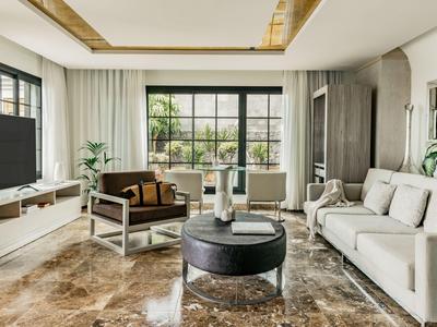 Modern living room with large windows, gray sofa, armchairs, and round coffee table.