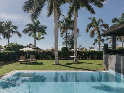 Swimming pool with shaded terrace and palm trees in hotel garden on sunny day
