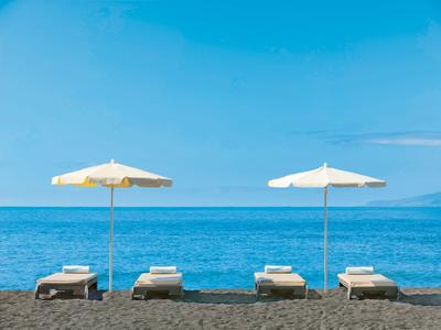 Four sun loungers with umbrellas on the beach by calm sea under clear sky.