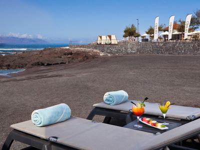 Lounge chairs with towels and drinks on black sand beach under clear sky.