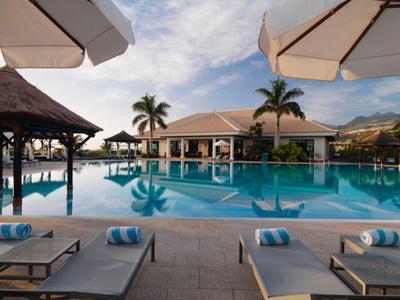 Resort pool area with sun loungers, palm trees, and a large water pool under a blue sky.