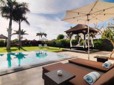 Pool area with lounge chairs, umbrellas, and tropical garden under clear sky.